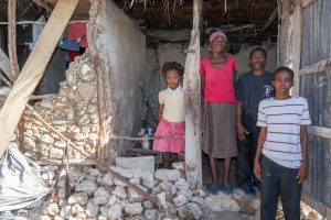 Family a mother and father and two children stand in the door of their destroyed home