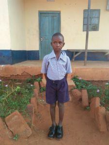 Mwendo John outside of his school. He needs your support to continue his education.