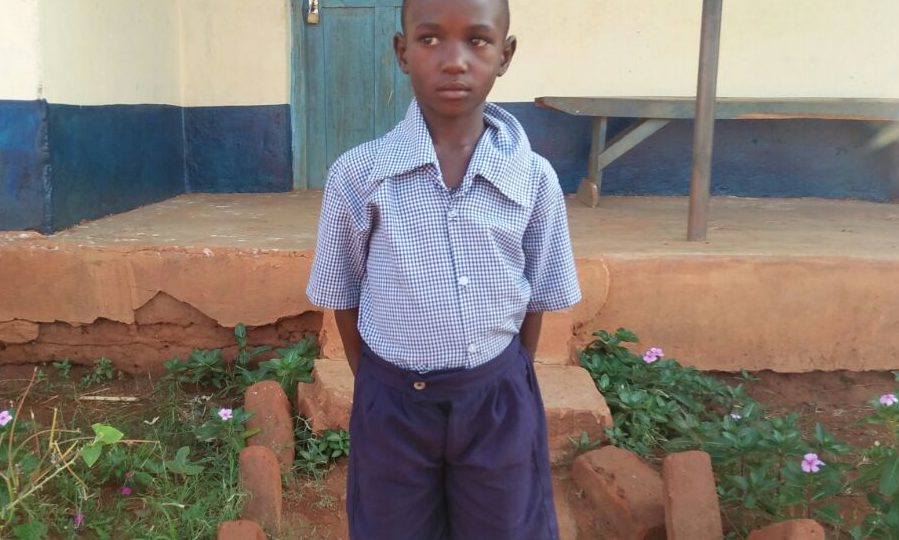 Mwendo John outside of his school. He needs your support to continue his education.