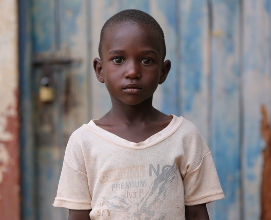 Child stands in front of a old wood door. He is an angel.