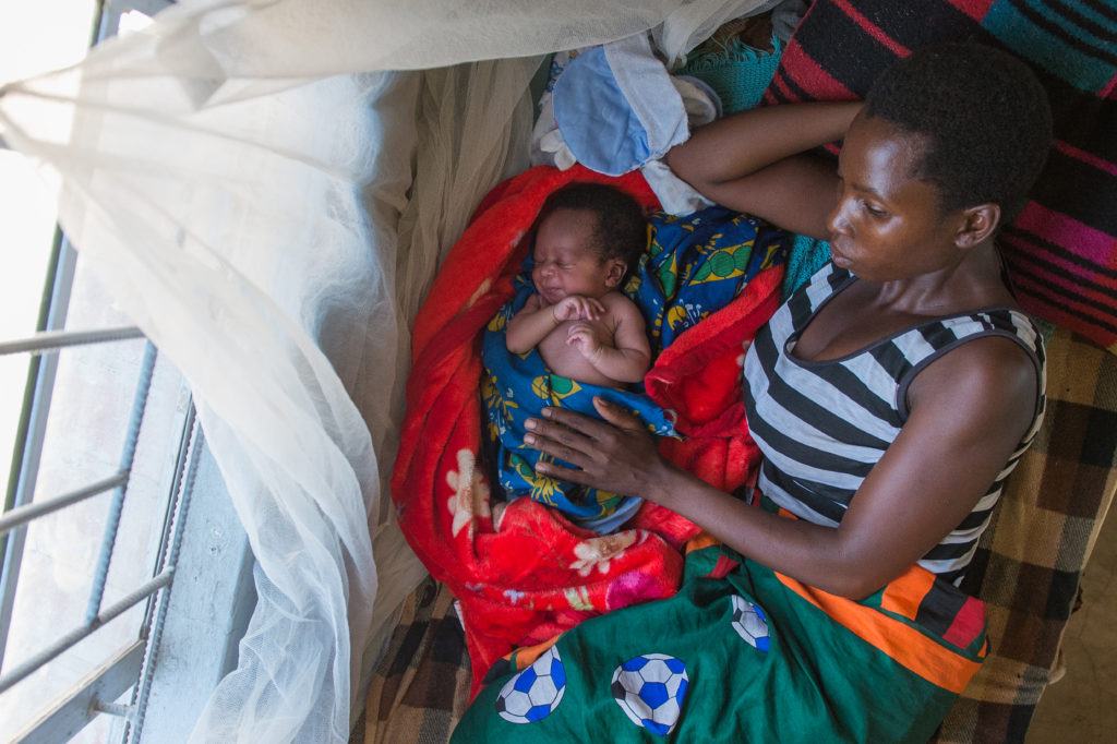 mother lying with infant under malaria net