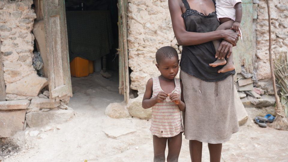 Dieukine standing next to his mom, looking a little bit shy outside of their home in Haiti.