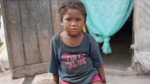 Michael sits in front of his family's home wearing hand-me downs from his older sister.