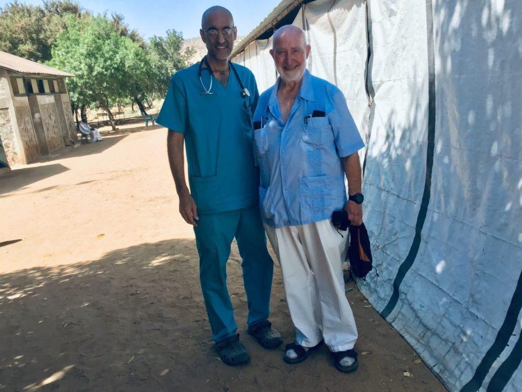 Dr. Tom with Dr. Harry in South Sudan. They stand in the shade outside.