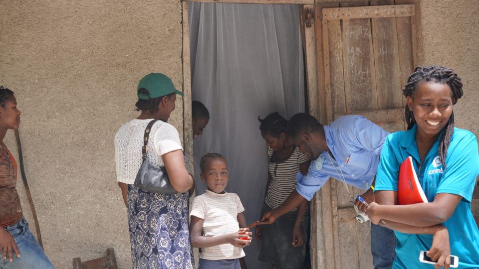 Nadia outside her home with volunteers and her family standing around.