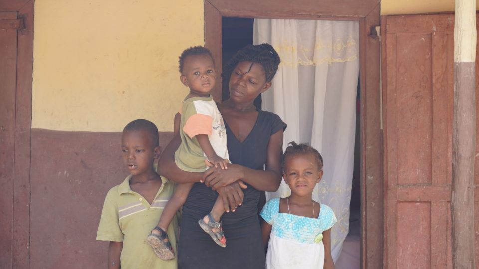 Stevenson held by his mom and with his two siblings in front of their house in Haiti.
