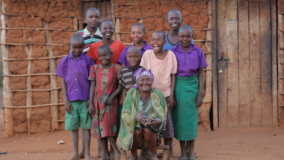 Grandma Grace and her grandchildren in front of their mud home