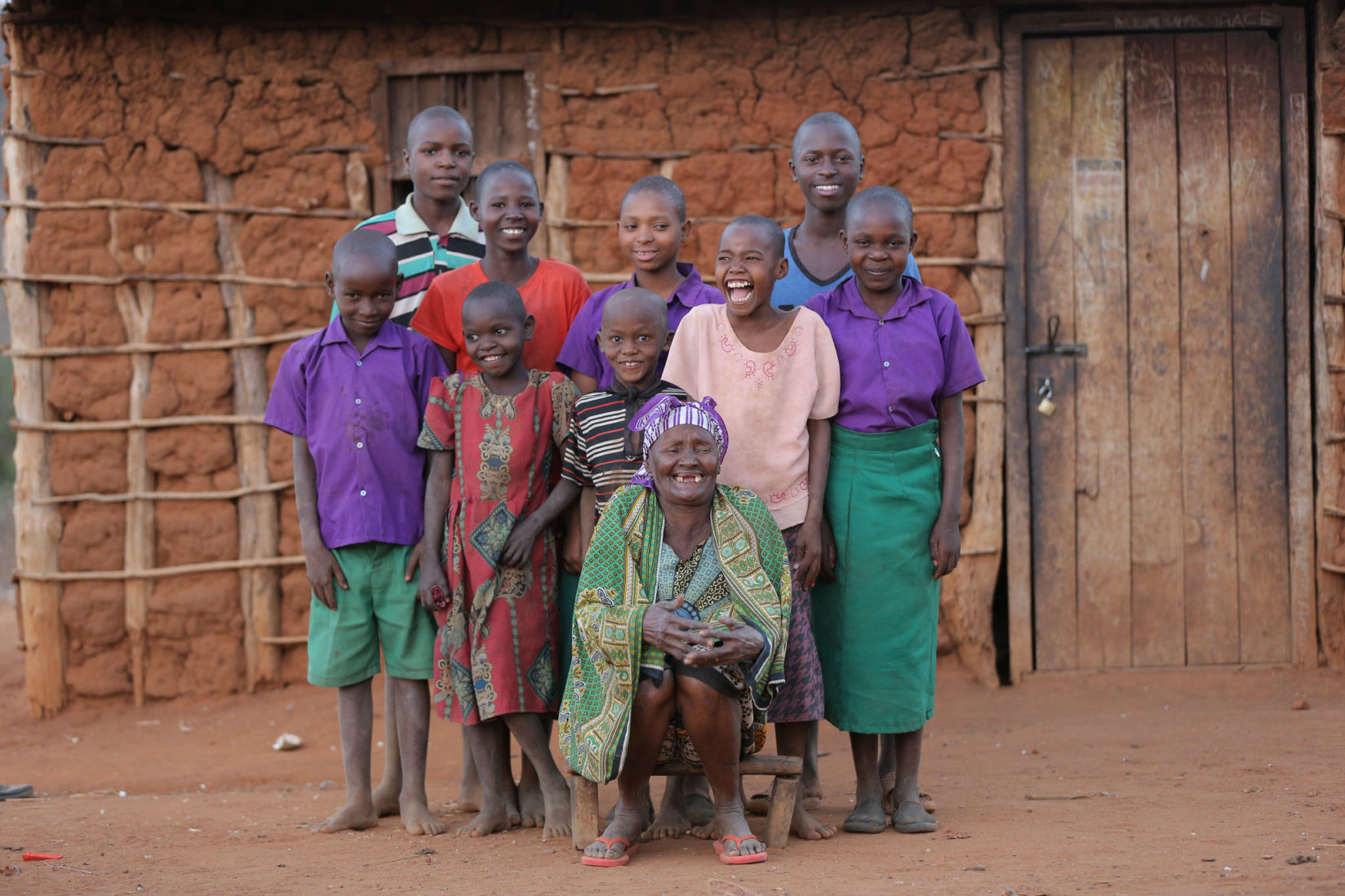 Grandma Grace and her grandchildren in front of their mud home