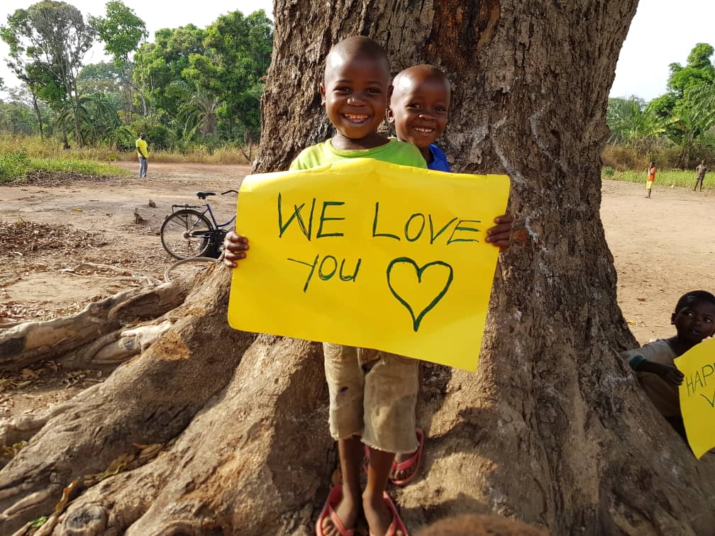 Boy from South Sudan with friend holding Valentines Day sign