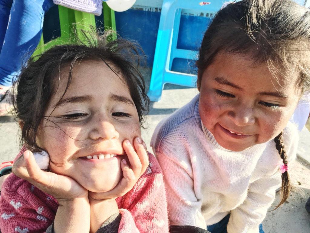 Two little girls in Peru, sitting beside one another and smiling 