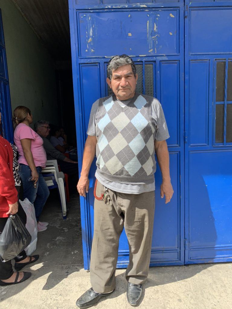 Image of a patient at the Santa Isabella Clinic. He stands in front of a blue door