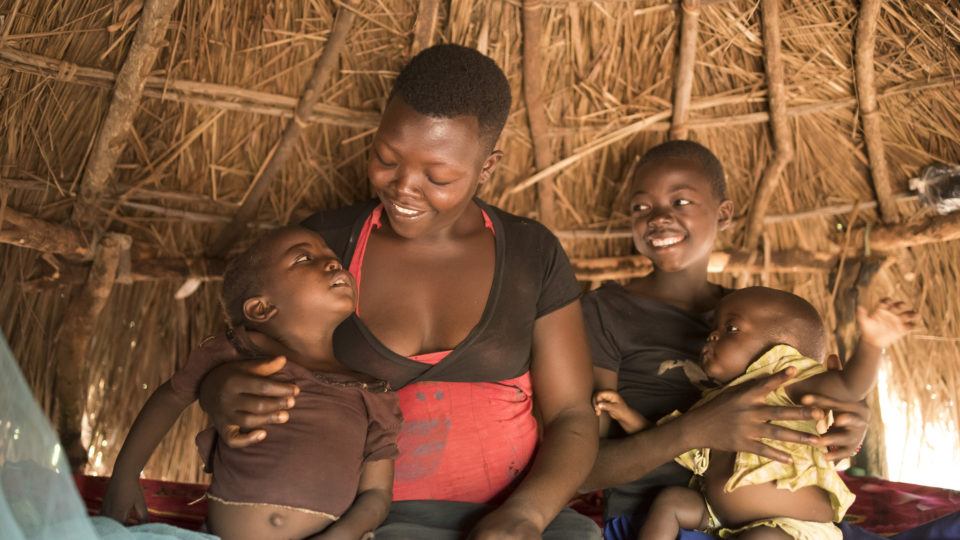 A mother from South Sudan sits in her home smiling at her children