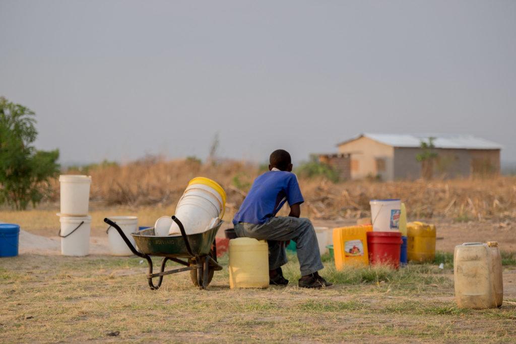 a young boy in Zambia sits with his head in his hands facing away 