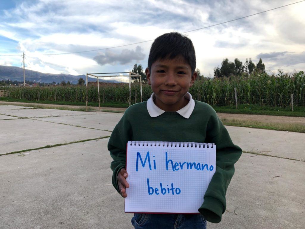 Young boy from Peru shares that his little brother makes him happy. He writes his response on white notebook 