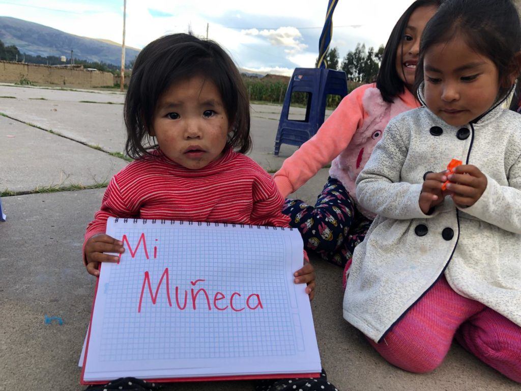Little girl from Peru shares that her doll makes her happy. She writes her response on a white piece of paper 
