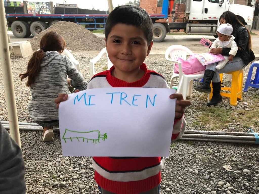 Young boy from Peru says that his toy train makes him happy. He holds up his response on a white piece of paper. 