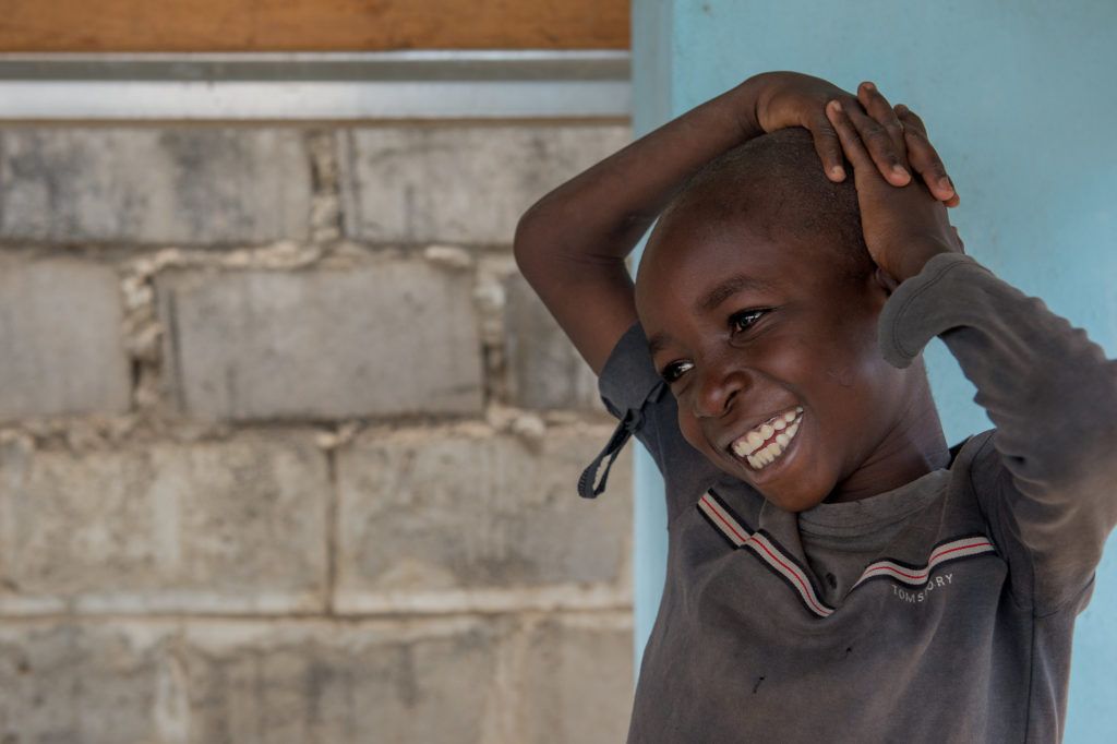 A little boy smiles with his hands on his head