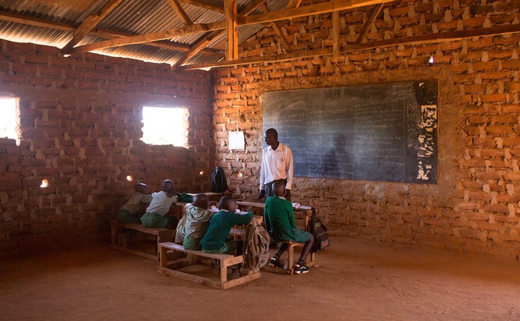 A teacher teaching his students. They are in a classroom made of brick