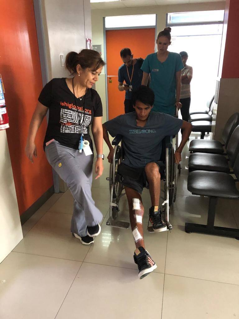 A staff member helps a patient in a wheelchair. In the background is Jessica - a cmmb volunteer nurse 