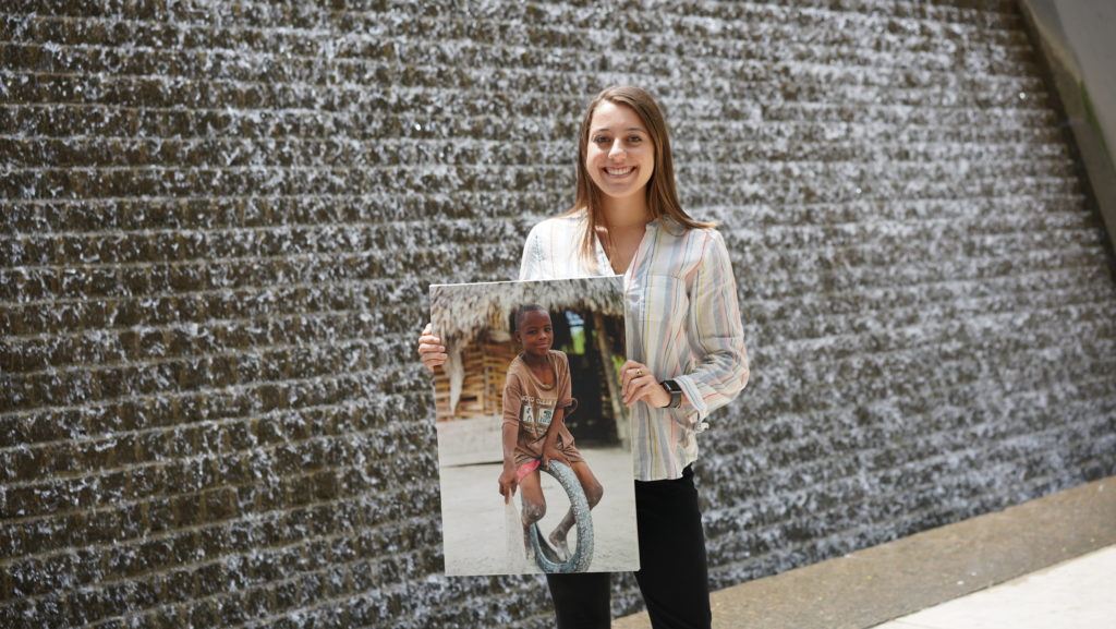 Carley - a cmmb intern poses outside with an image of a child we serve 
