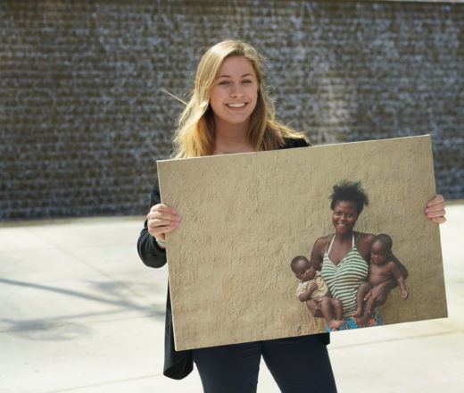 Chloe, a CMMB intern poses outside with a photo of individuals we serve