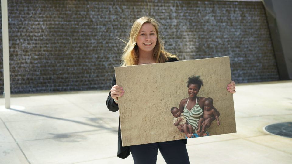 Chloe, a CMMB intern poses outside with a photo of individuals we serve