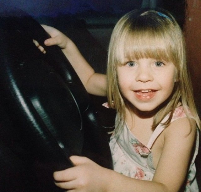 Image of Chloe, a cmmb intern as a child. She sits behind the wheel of a car pretending to steer 