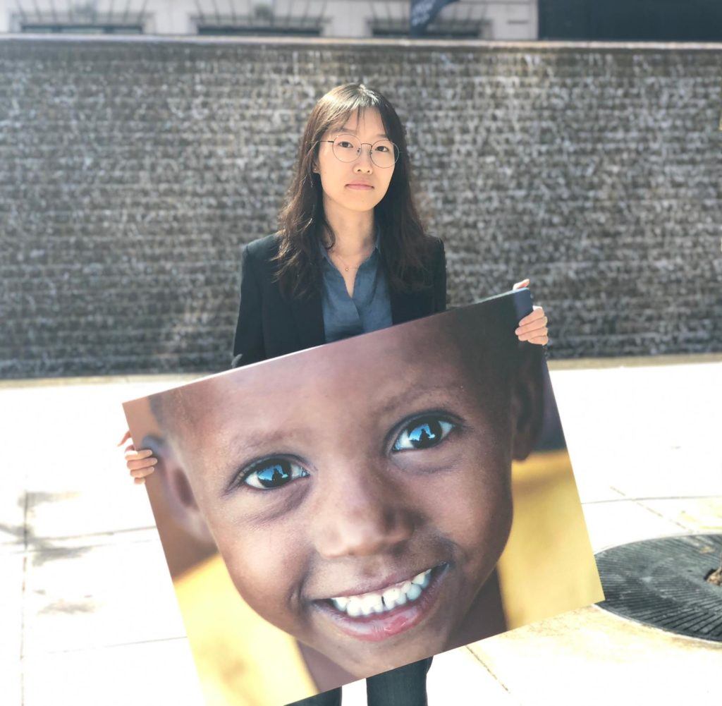 Chu, a summer intern, poses outside with a canvas image of one of the children we serve 