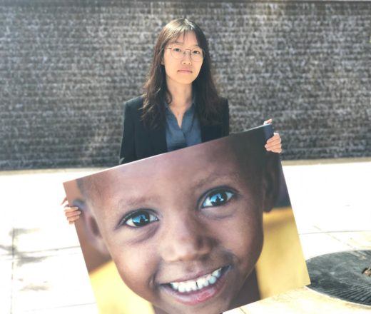 Chu, a summer intern, poses outside with a canvas image of one of the children we serve
