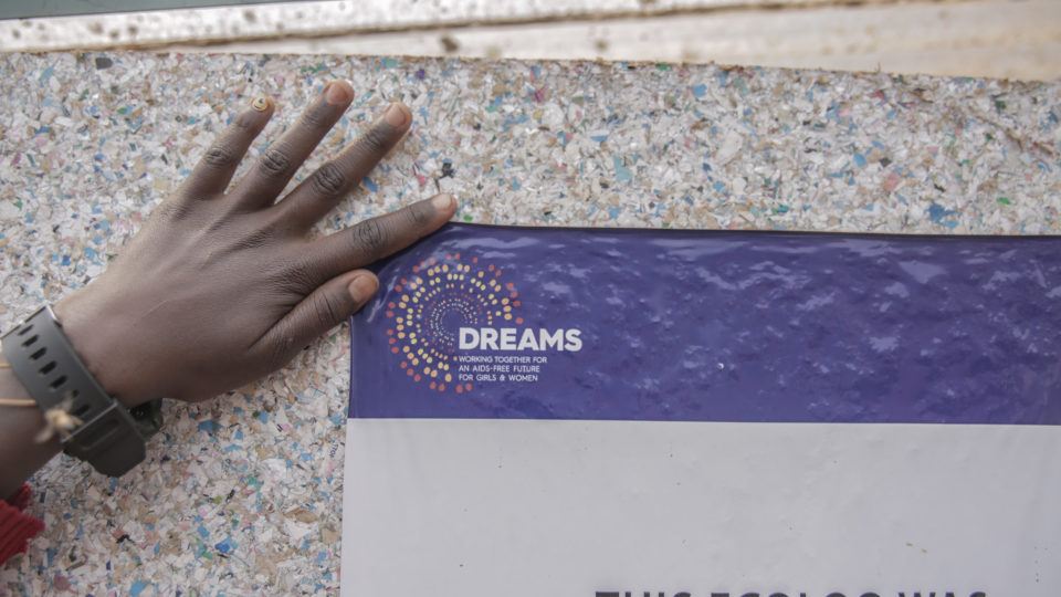 A hand holding up a DREAMS sign agains a gray background