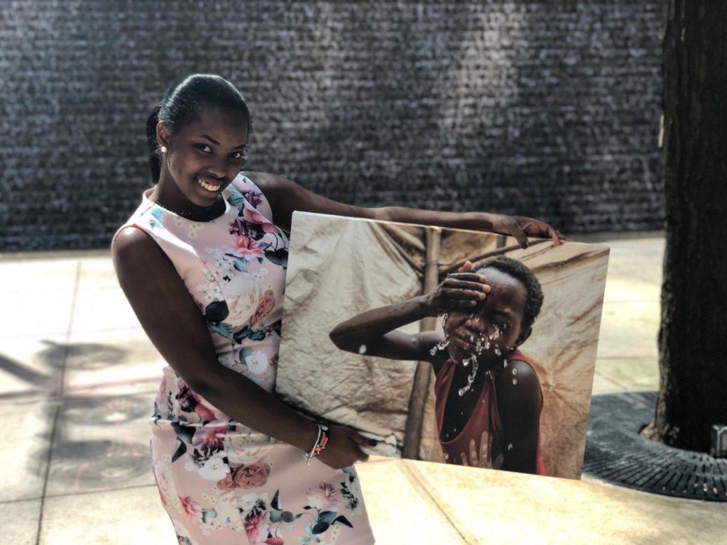 Edna Nthenya, a CMMB intern posing outside with an image of an individual we serve 