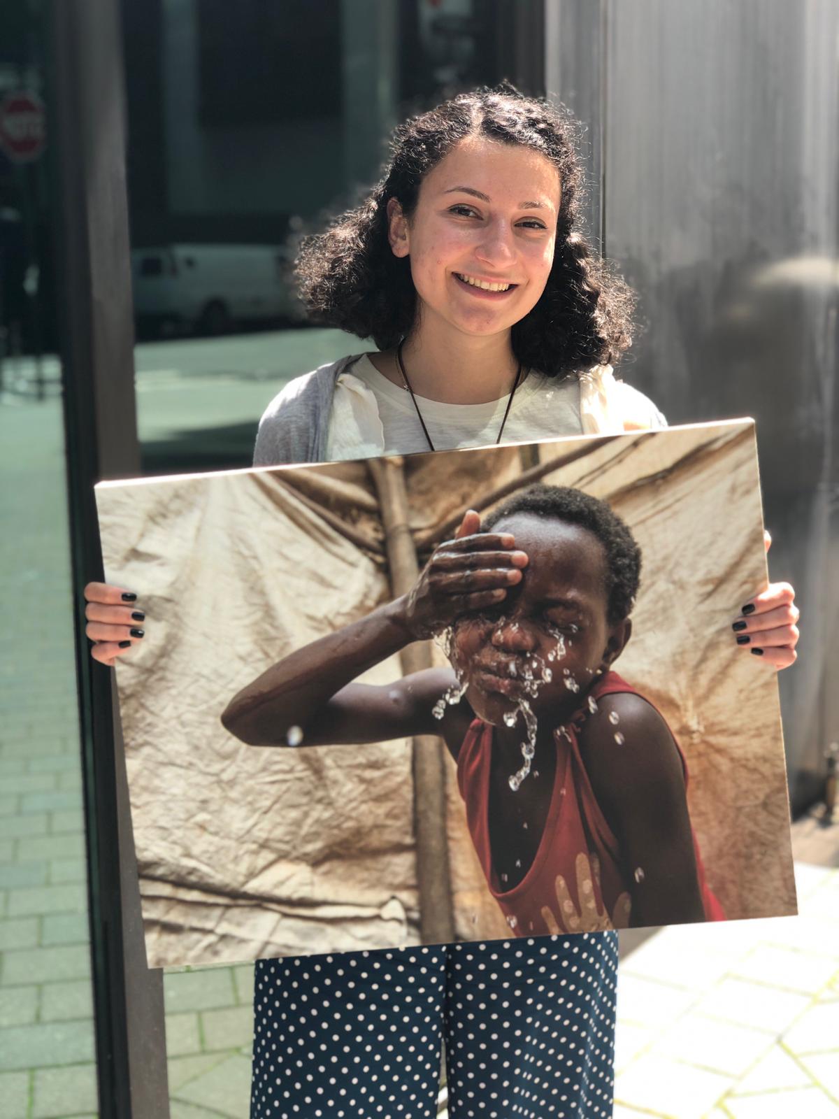 Grace is a CMMB intern. She poses outside with a canvas image of a child we serve in the field