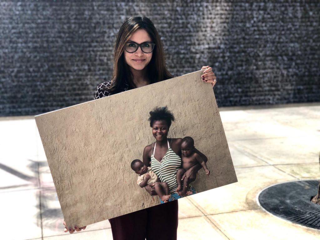Marisha our summer intern poses outside with a canvas photo of a mother served in the field