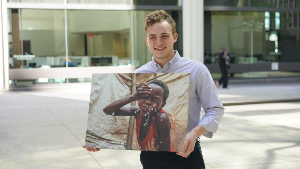 Nicholas is a CMMB intern who poses outside with a canvas image of an individual we serve 