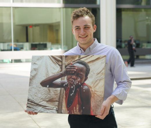 Nicholas is a CMMB intern who poses outside with a canvas image of an individual we serve