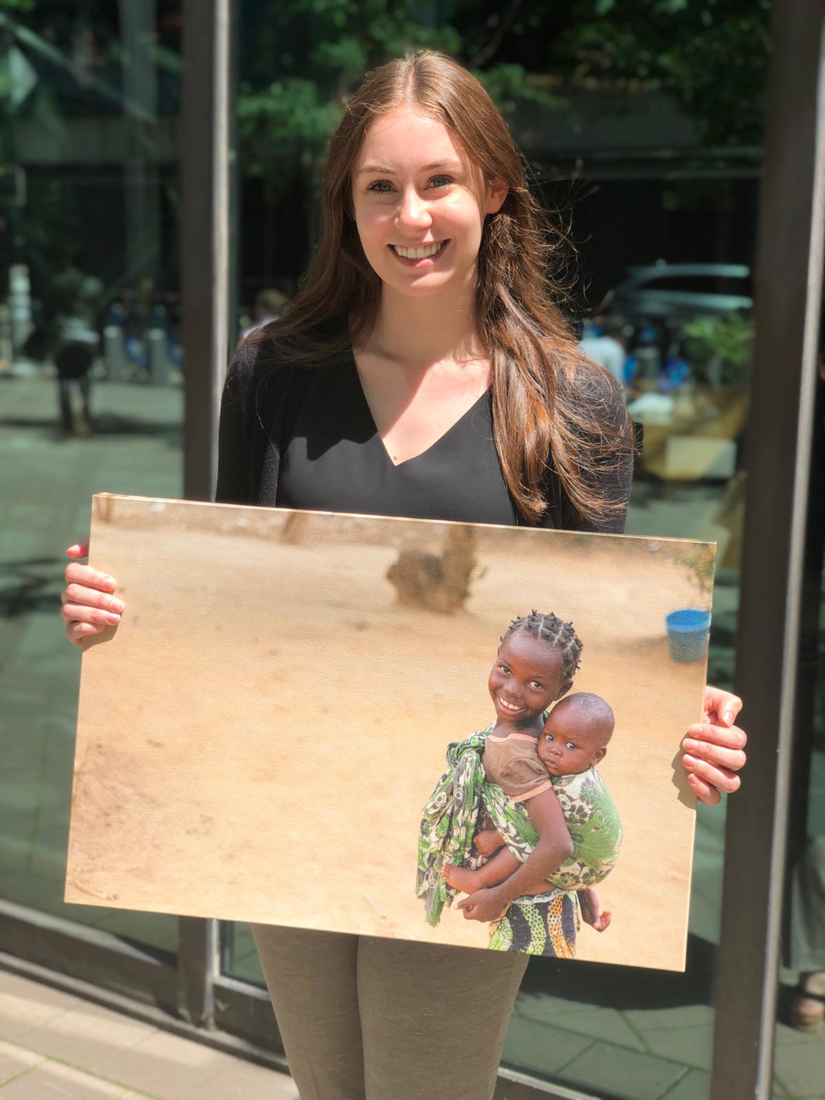 Nina is a CMMB intern and she poses outside with a canvas image of two children we serve in the field