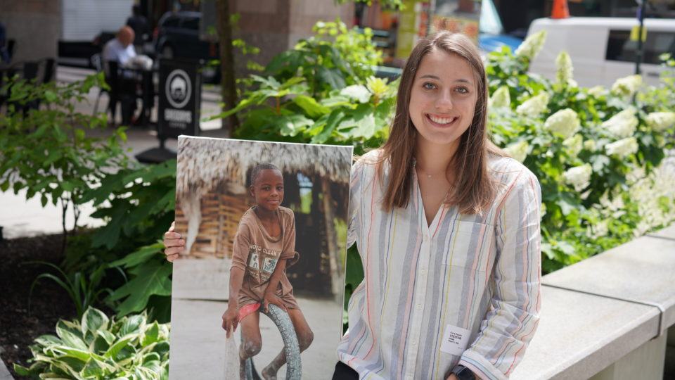 Carly Fassler outside holding a canvas photo of a child served in the field by CMMB