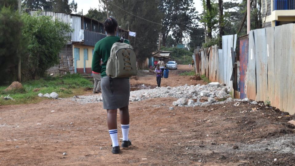 A young girl enrolled in our DREAMS project walks to school. Her backpack is on one shoulder as she walks to school. She is a part of the DREAMS mentorship program.