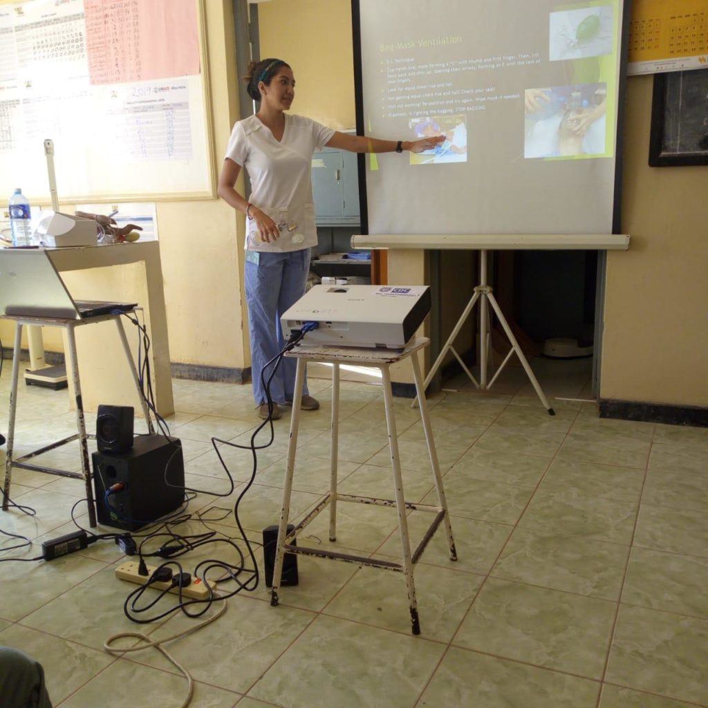 Samantha stands in front of a projection screen presenting to nurses 