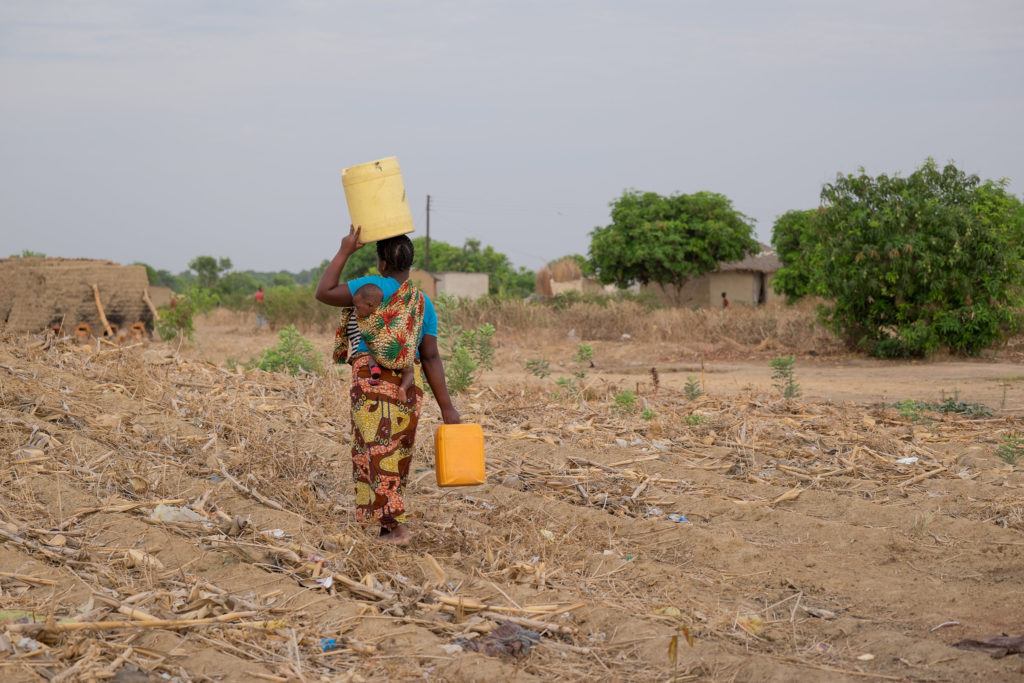 A woman carries water over head and by her side. She carries a baby with her as well