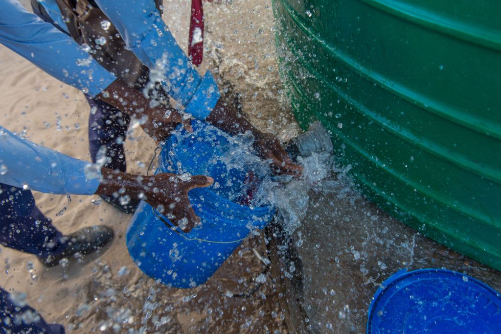 Children collect water from. It is spraying around the bucket