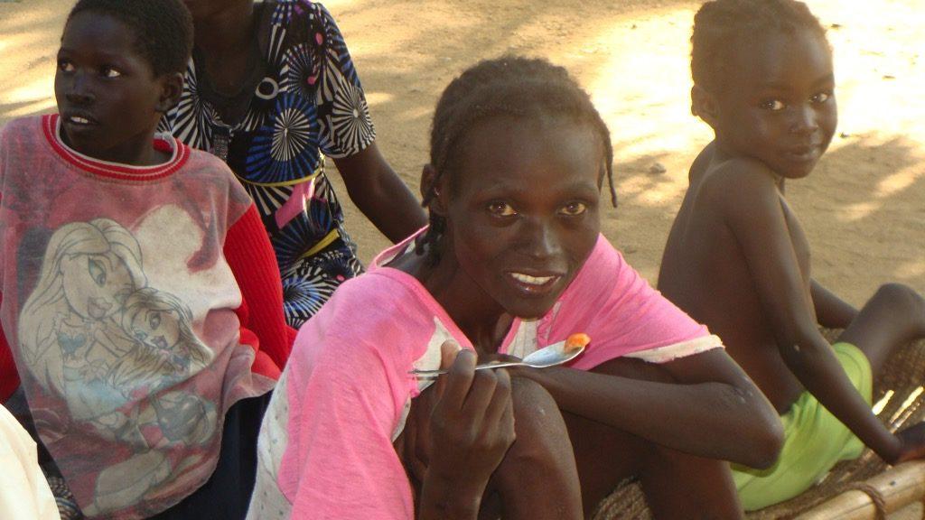 A malnourished woman in Sudan holds a spoon with food on it. 