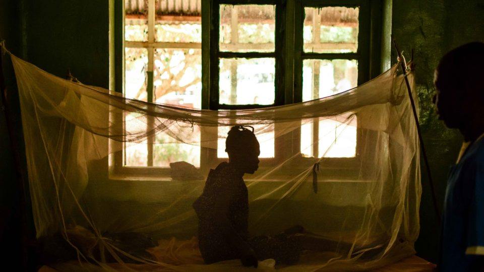 Woman sitting under a malaria prevention net in a dark hall of the St. Therese Hospital in South Sudan