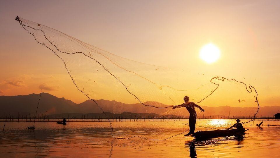 fishermen throwing a net in the water at sunset
