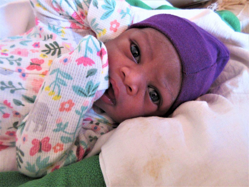 A newborn girl wears a purple hat