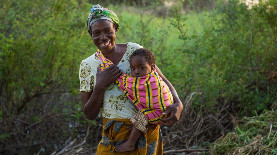 A mother in Zambia holds her baby while standing in her garden. At CMMB we are celebrating Mother's Day