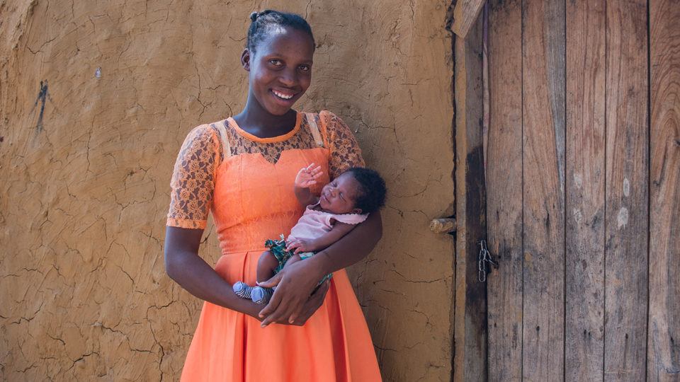 A mother in an organge dress holding her infant in Mwandi, Zambia in October 2019.