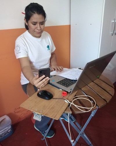 A community health worker before a computer with a phone during COVID-19 reaching the community through telecounseling in June 2020.