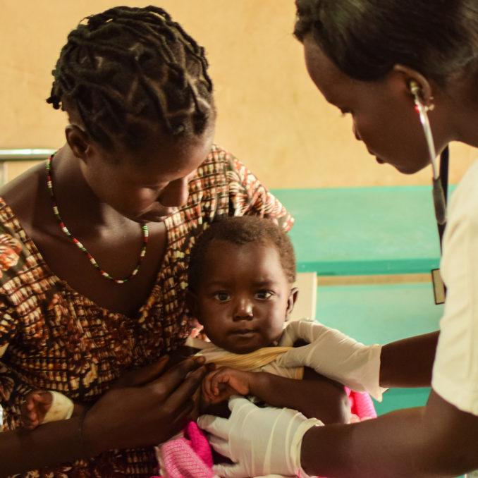 A nurse serving a child while being held by mother in South Sudan in March 2019