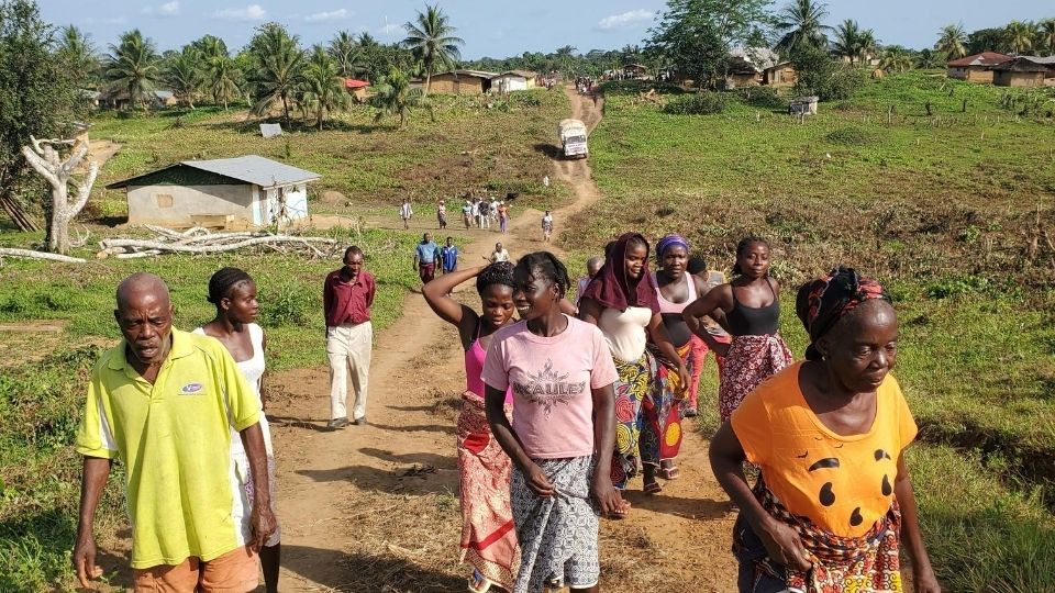 A group of people walk down a dirt road in a village of Liberia